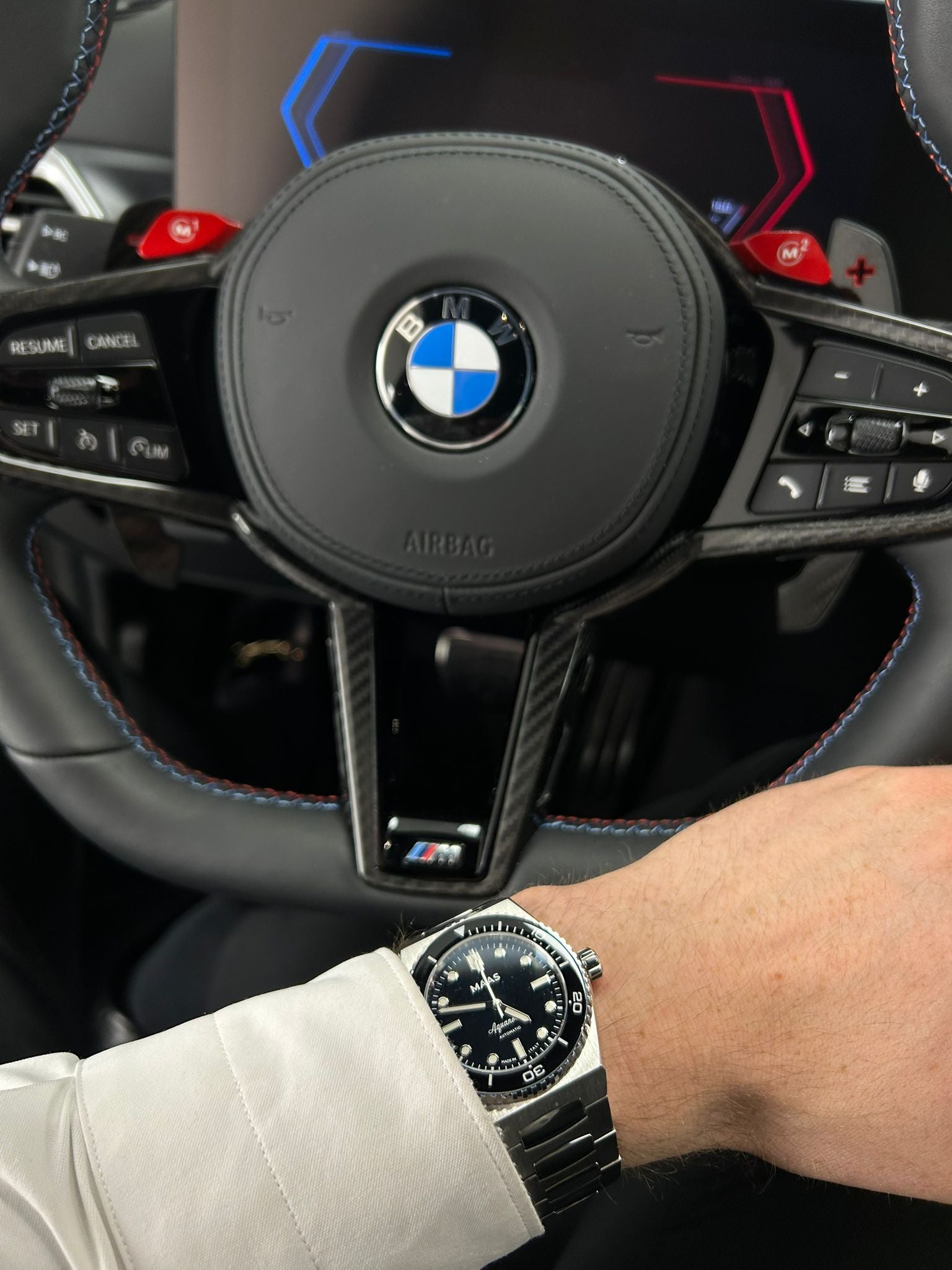 Steering wheel with BMW logo and a person wearing a watch in a car interior.