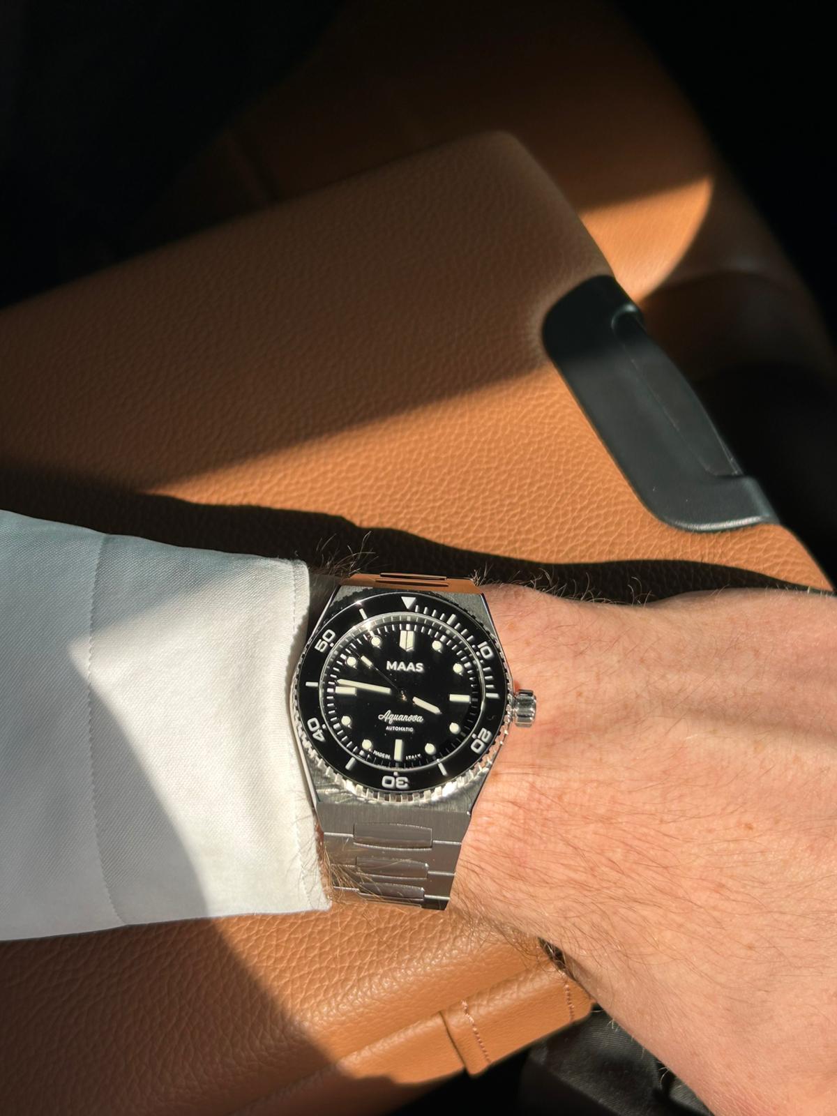 Black wristwatch with silver case on a person's wrist, sitting on a brown surface.