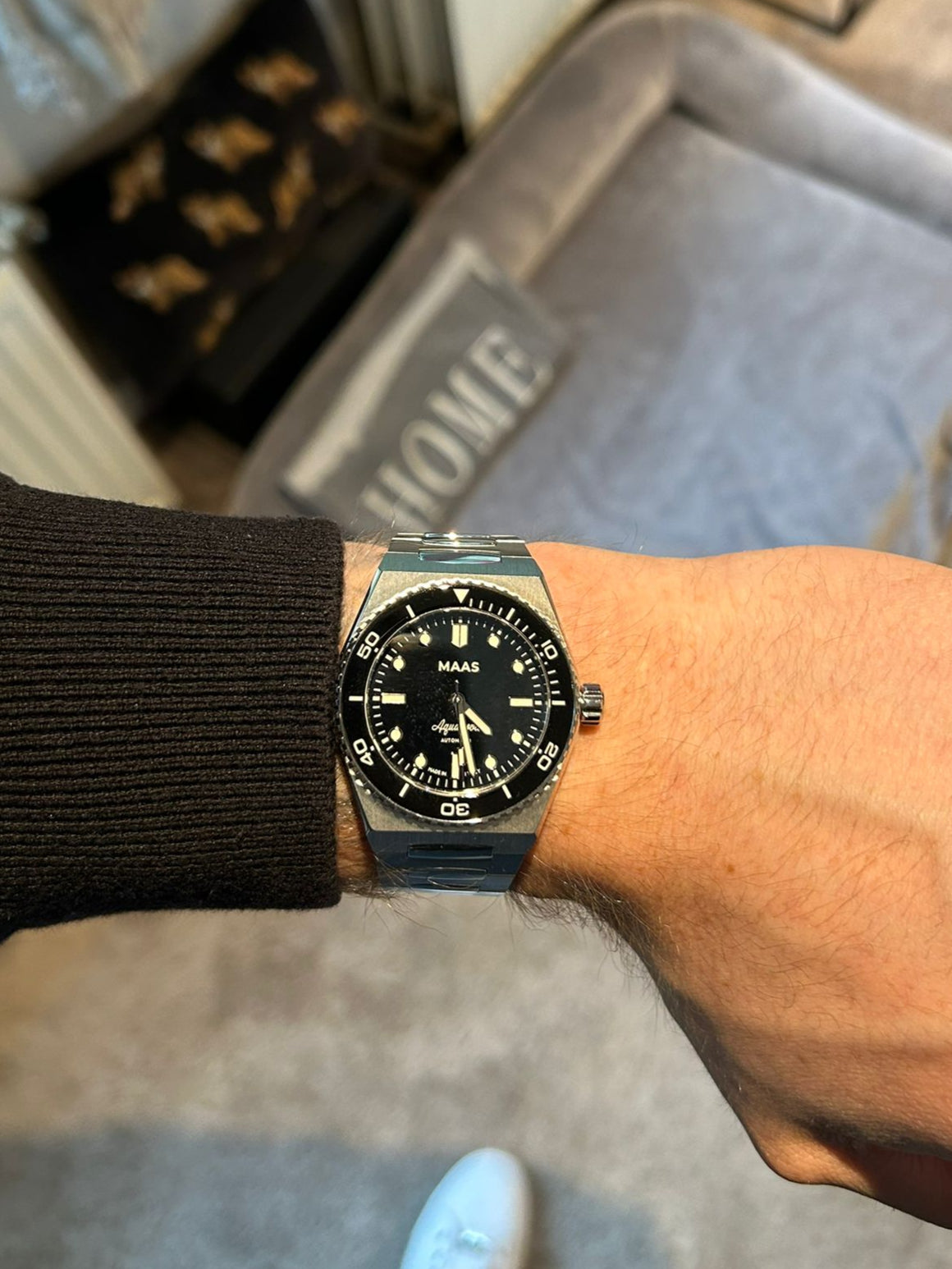 Person wearing a black wristwatch with a blurred indoor background