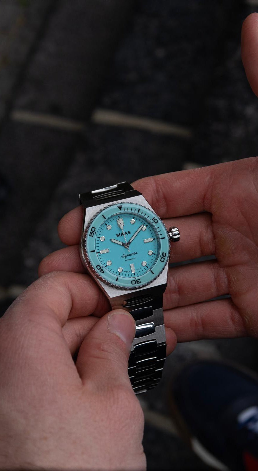 Hand holding a watch with a blue face against a blurred background